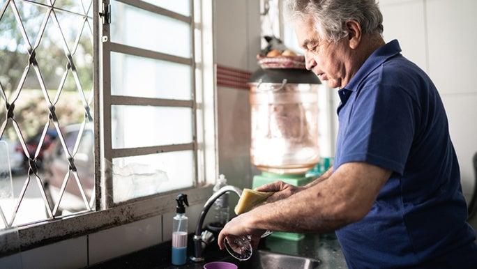 A senior man is washing his hands at a sink